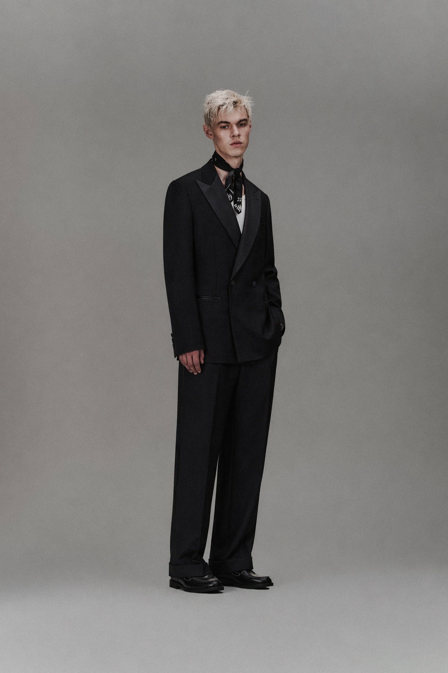 Person wearing a black dinner suit and tie against a gray background