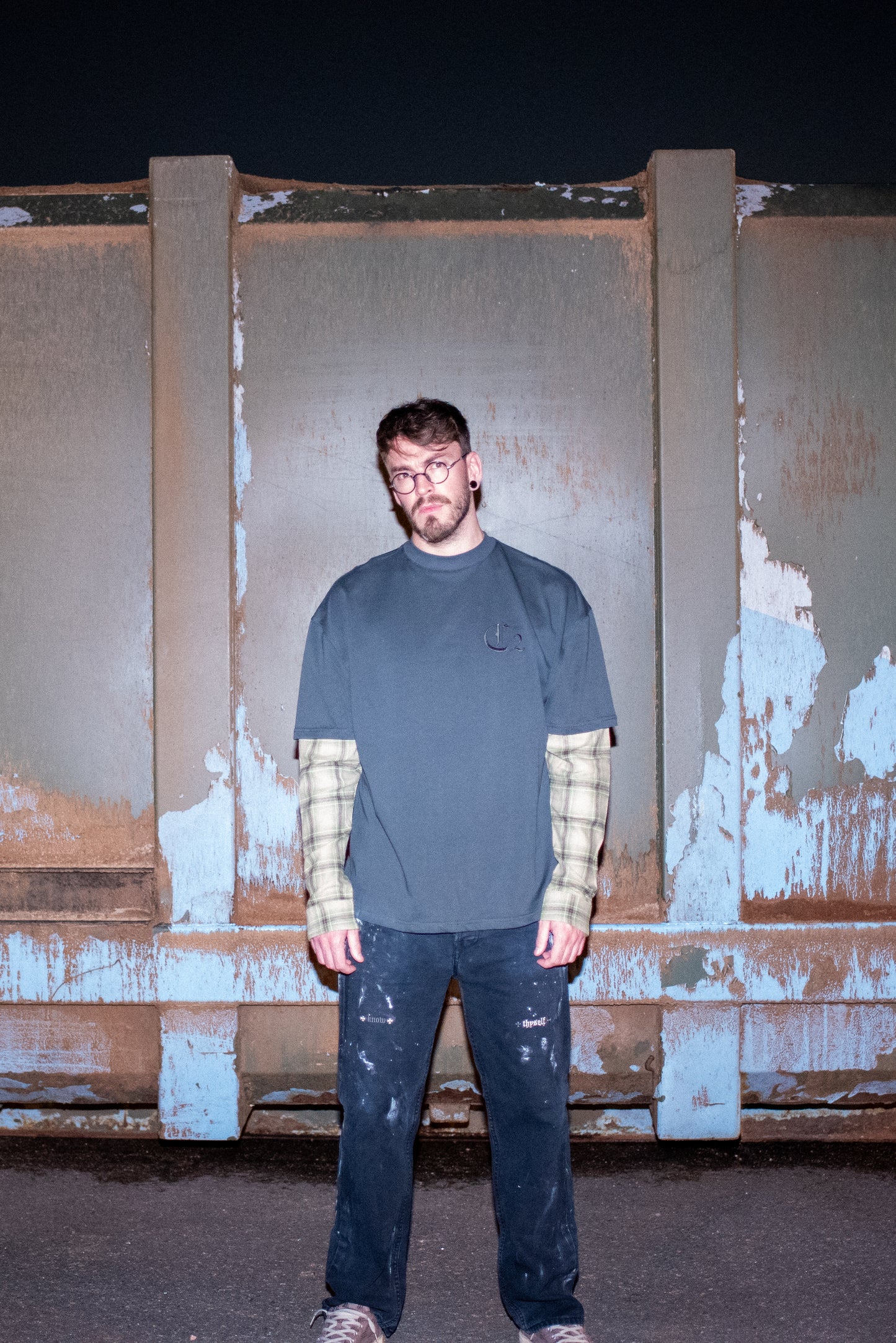 Oversized T-shirt in grey with plaid sleeves worn by model in Chrome Hearts Glasses, customised painted levi's jeans and Baleniaga shoes, shown from the front